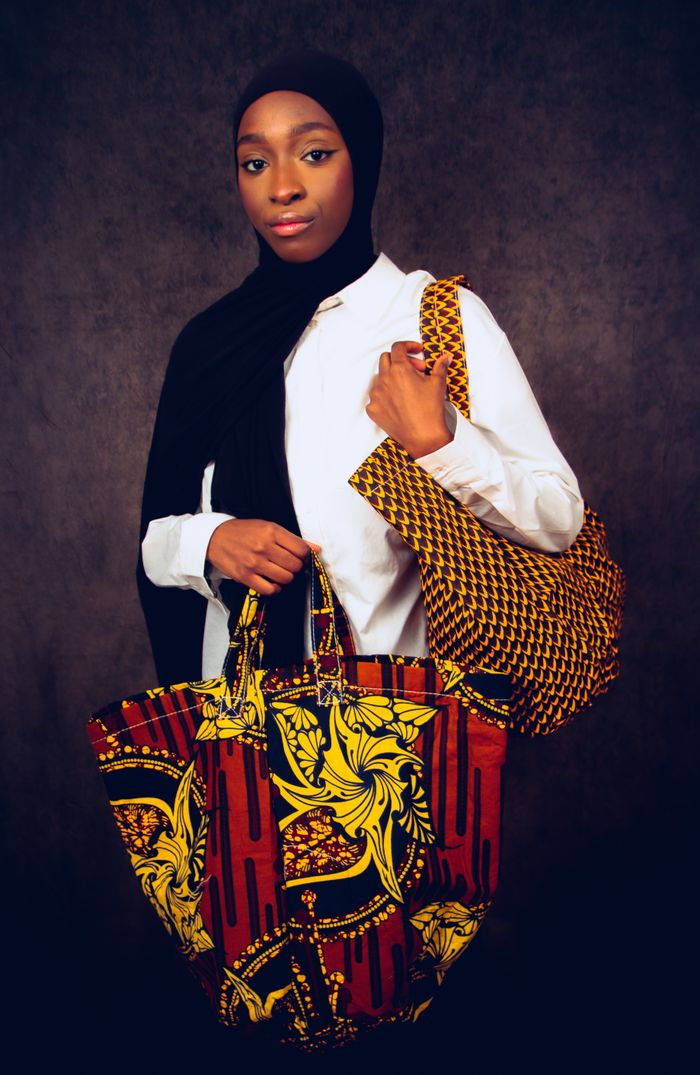 Elegant woman in hijab holding vibrant patterned tote bags against a studio backdrop.