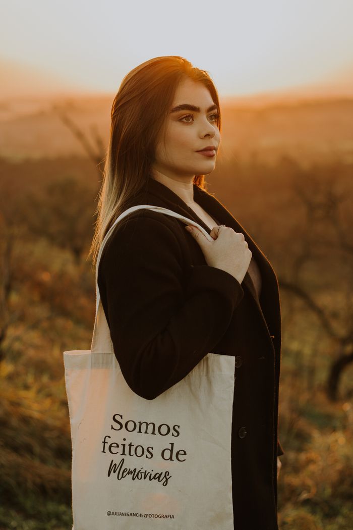 Woman standing with a tote bag during a beautiful sunset outdoors, conveying a serene mood.