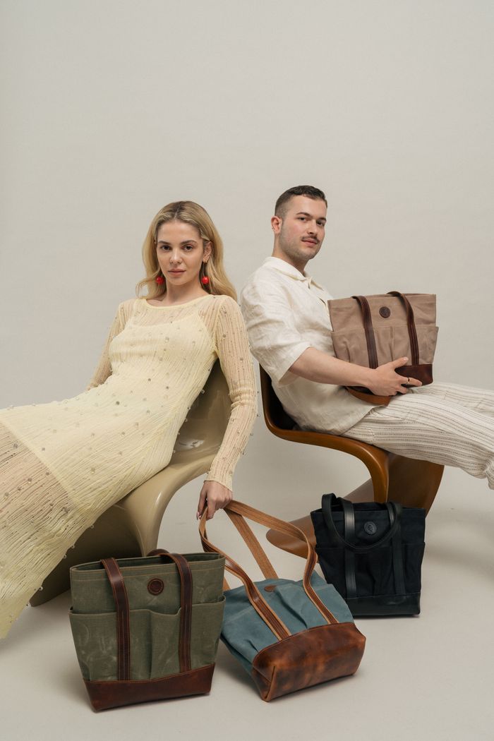 Fashionable duo posing indoors with stylish tote bags, showcasing modern outfits.