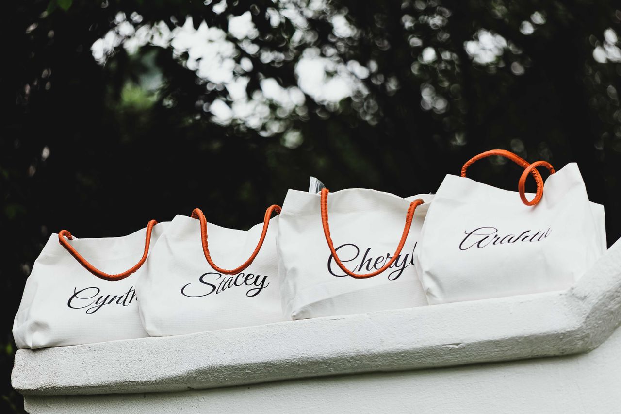 team-01 Four personalized tote bags with names and orange handles on display outdoors.